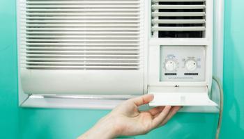 Eine Hand öffnet das Bedienfeld zu einer Klimaanlage