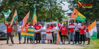 Gruppe junger Menschen bei den „West Africa Youth Days Accra 2026“, die im Freien gemeinsam westafrikanische Flaggen und Veranstaltungsschilder präsentieren.